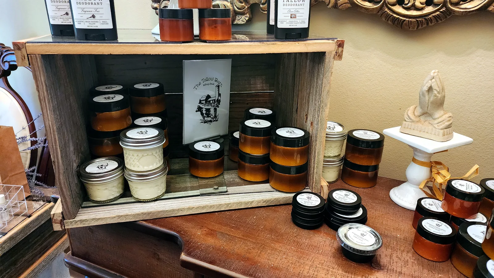 Tallow balm jars and product tins arranged inside a rustic shelf display.