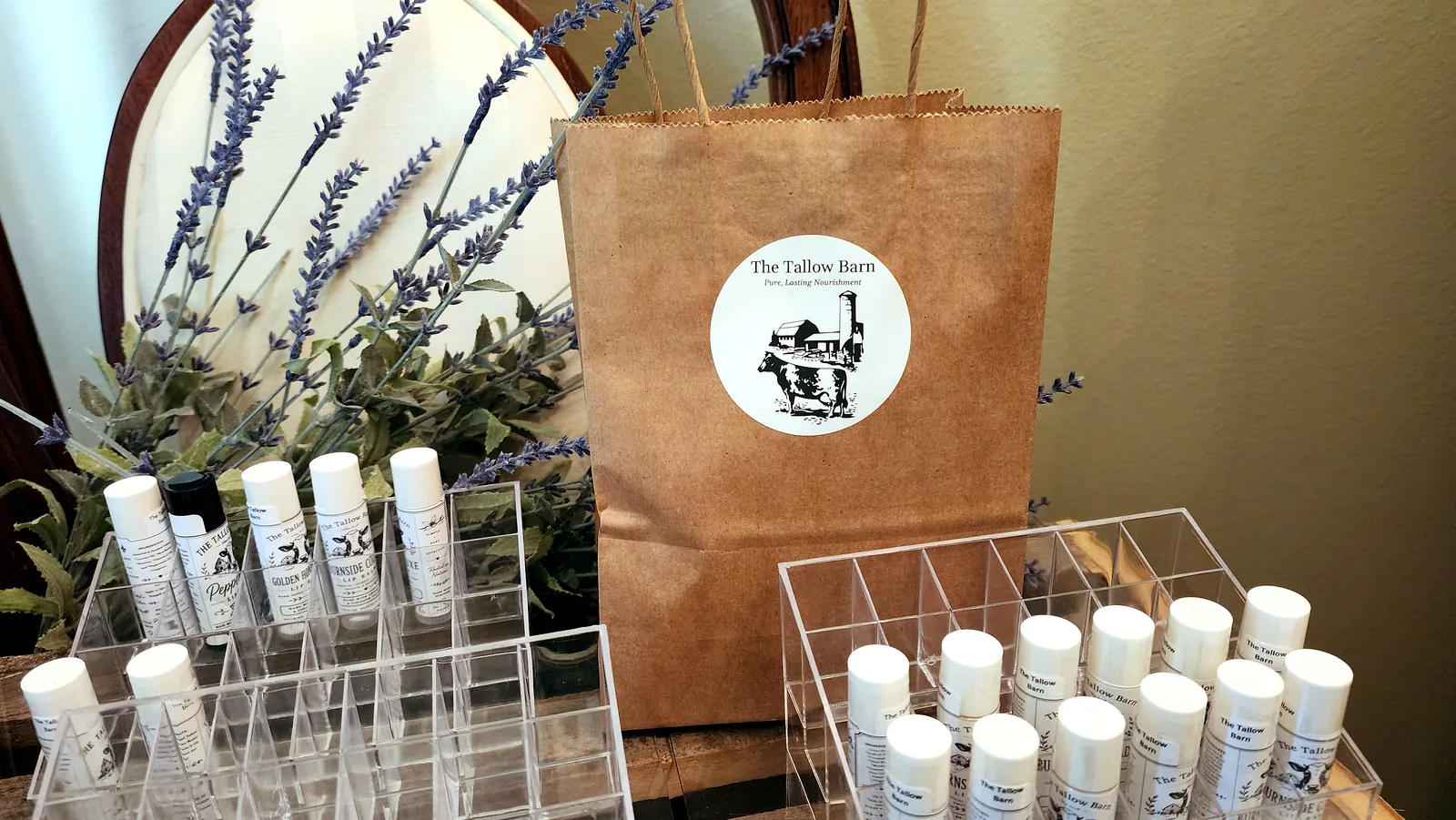 A branded The Tallow Barn kraft bag displayed behind rows of handmade lip balms.